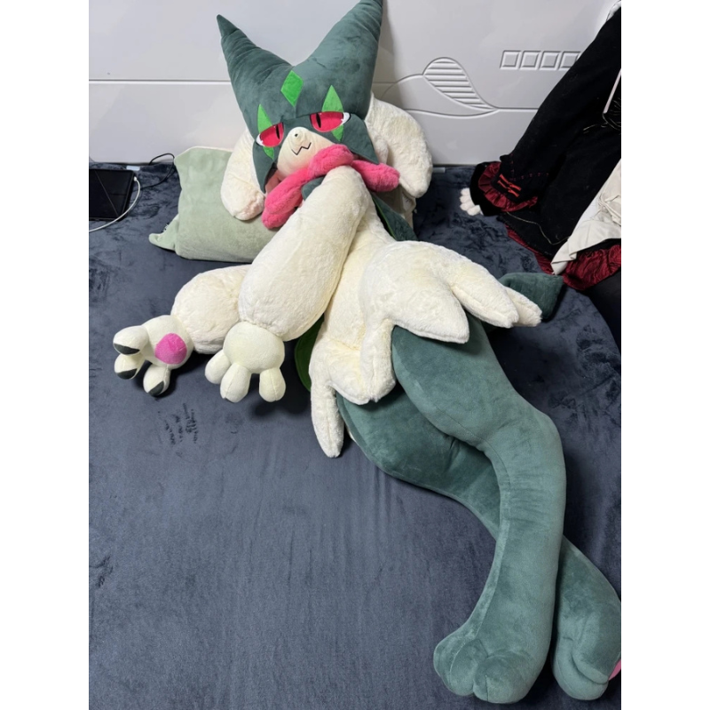 Pokemon Meowscarada Plush Pillow Stuffed Toy A large plush toy of a green and cream-colored dragon-like character with red eyes and a pink scarf, posed on a dark gray bed with pillows and other bedding visible.