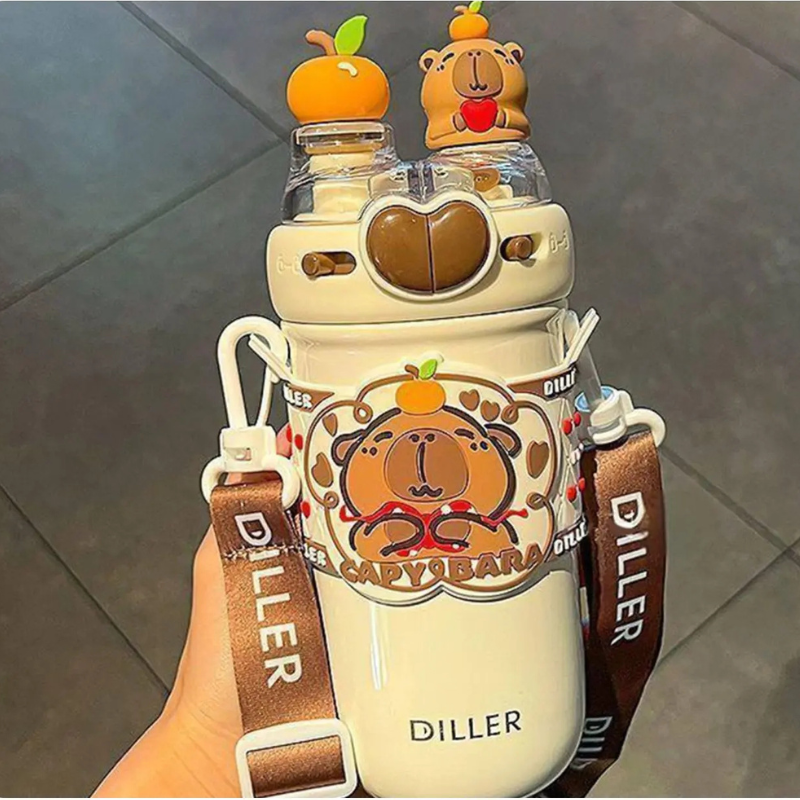 Capybara Insulated Tumbler – Cute Cartoon Water Bottle A hand holds a white insulated water bottle with a brown strap and cartoon capybara design. The bottle has a clear lid with two small capybara figures topped with orange fruits, and the word DILLER is visible on the strap and bottle.