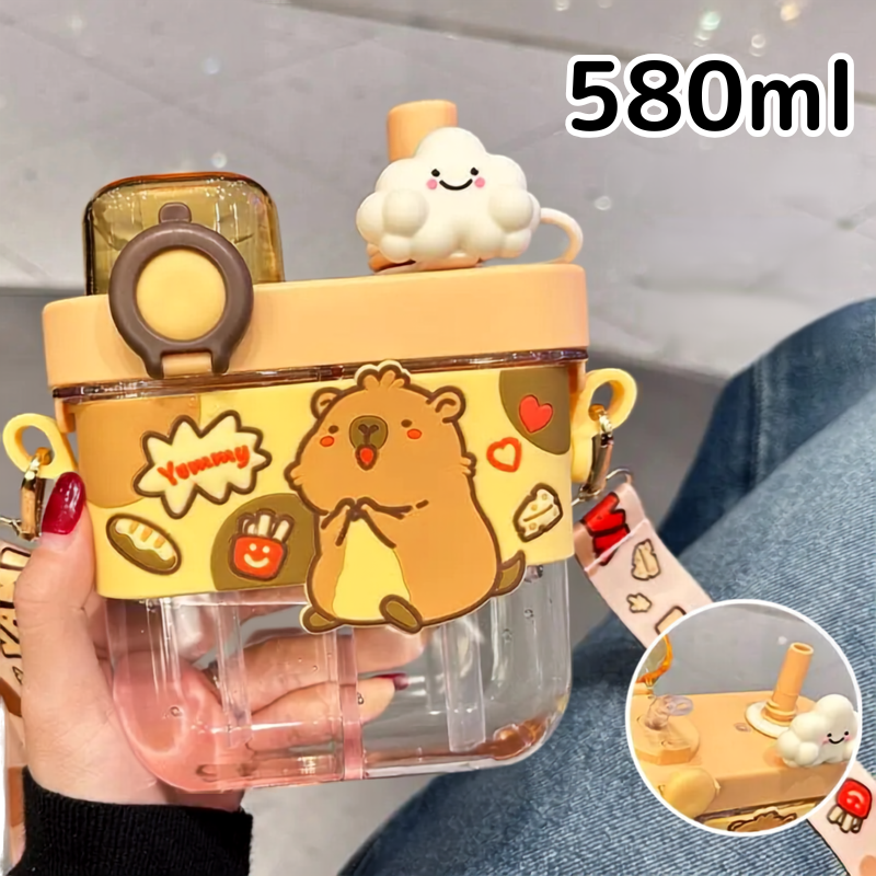 Capybara Kids Water Bottle – Cartoon Straw Cup A person holds a large clear plastic water bottle with a yellow lid and strap, decorated with cute cartoon graphics including a brown animal character, hearts, and food motifs. The bottle has a text overlay reading '580ml' and a circular inset showing a close-up of the straw and cloud topper.