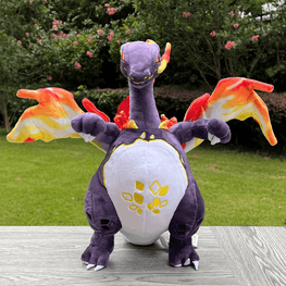 A plush toy of Charizard, the fire dragon from Pokémon, sitting on a gray wooden table with a green grassy lawn and bushes in the background. The toy is purple with a white belly, yellow accents, and orange and yellow wings.