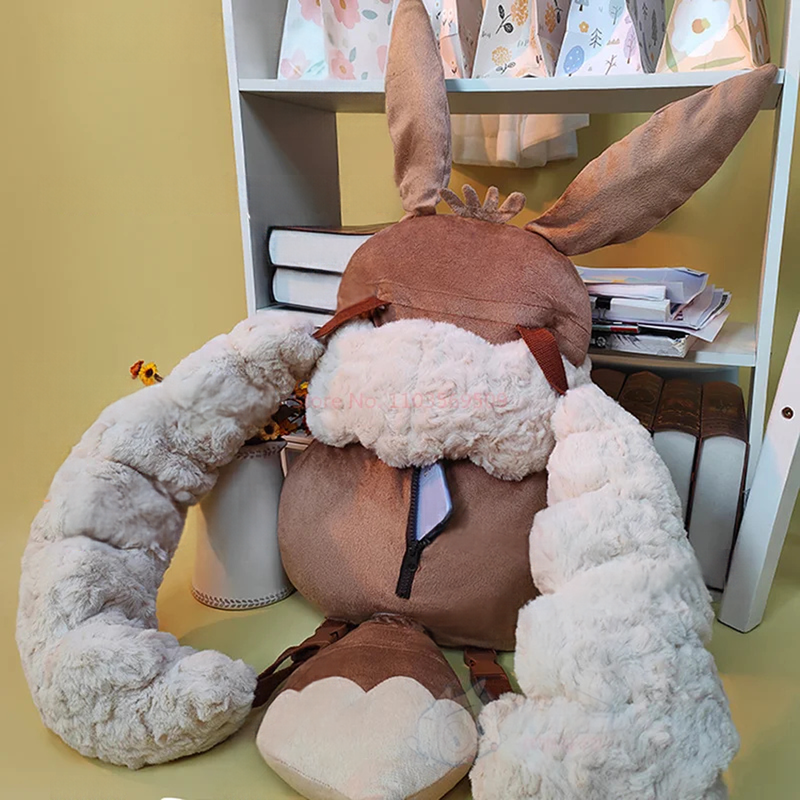 Eevee Plush Backpack – Kawaii Pokemon Cosplay Bag A plush bunny-shaped backpack or bag in brown faux fur with long white fluffy side flaps and a small black-and-white tie detail, photographed indoors against a yellow wall and white shelving.