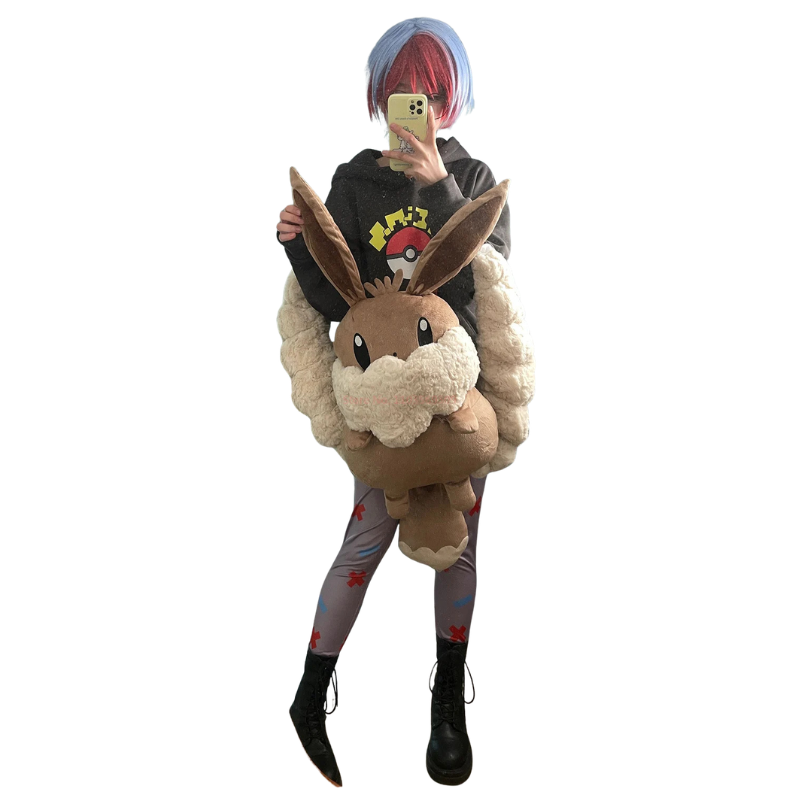 Eevee Plush Backpack – Kawaii Pokemon Cosplay Bag A person takes a mirror selfie wearing a full-body Eevee cosplay costume. The outfit includes a black hoodie with a yellow and red Eevee graphic, a large plush Eevee body, gray leggings with red leaf patterns, and black combat boots.