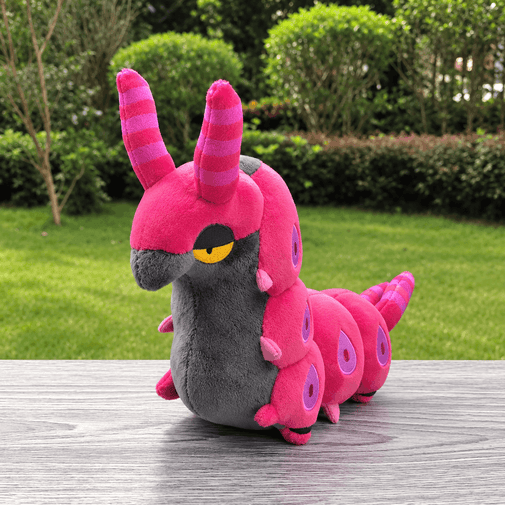 A pink and gray caterpillar plush toy with striped antennae and a yellow eye, sitting on a gray wooden table with a green grassy garden background.