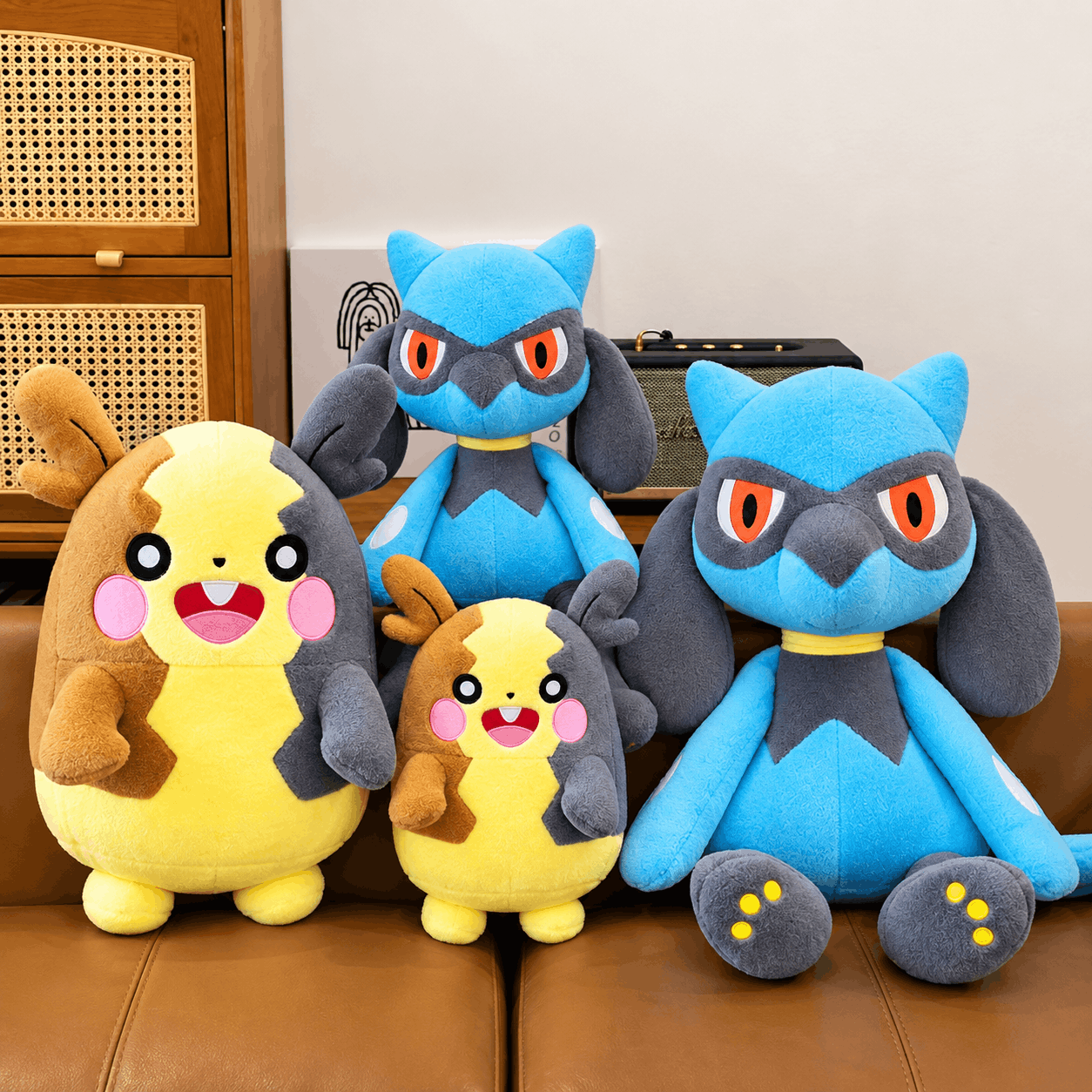 Four plush toy characters posed together on a brown leather couch in a real indoor room, with a wooden cabinet and wall visible in the background.