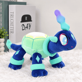 A plush toy turtle character in shades of blue, mint green, and light green, standing on a white faux fur surface with decorative books in the background.