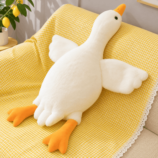 A plush white goose toy with orange beak and feet, posed on a yellow gingham blanket draped over a sofa in a bright indoor setting.