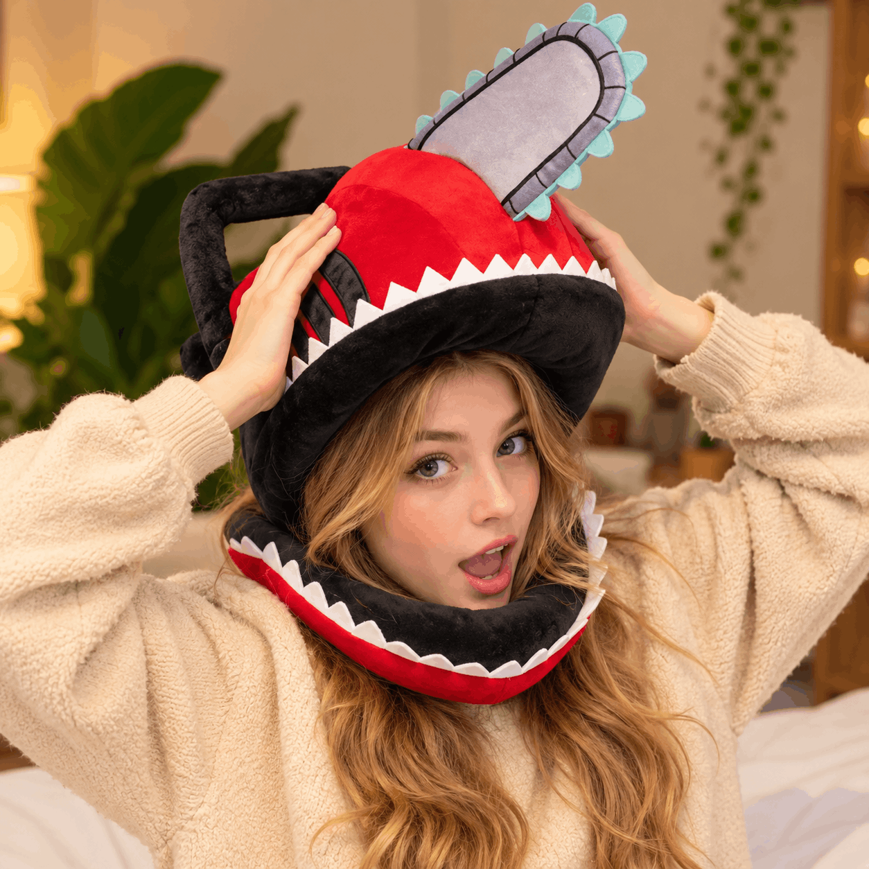 A woman wearing a plush chainsaw hood hat and a cream-colored fleece pajama top, adjusting the hat with both hands in a cozy indoor setting.