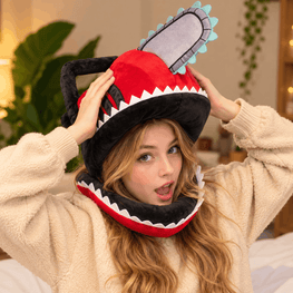 A woman wearing a plush chainsaw hood hat and a cream-colored fleece pajama top, adjusting the hat with both hands in a cozy indoor setting.