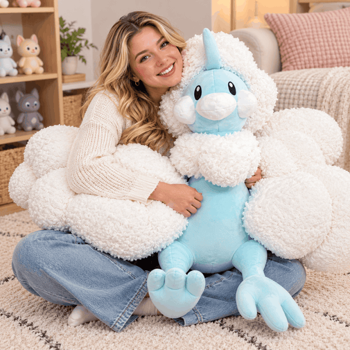 A woman sitting on a rug in a cozy living room setting, holding a large plush toy that combines a light blue body with fluffy white cloud-like wings and a matching white cloud-shaped pillow.