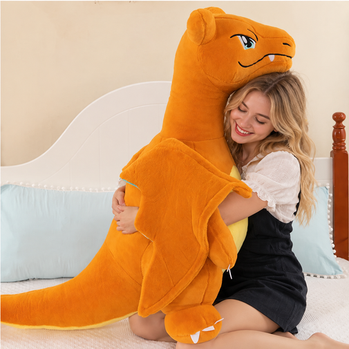A woman sitting on a bed hugging a large orange plush dragon toy with a cartoon face and wings.