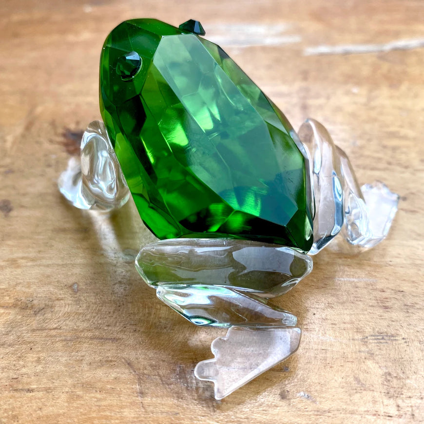 Crystal frog figurine with a green gem on a wooden surface