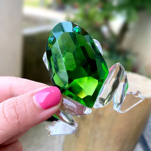 Green gemstone ring held by a hand with pink nail polish.