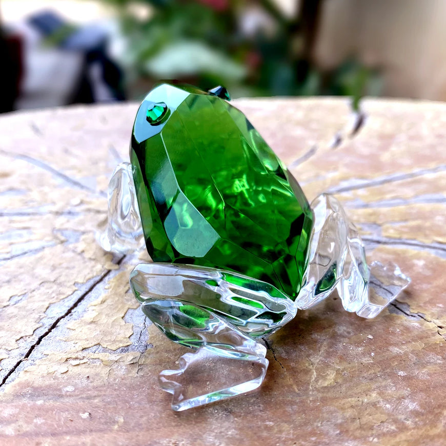 Green crystal frog figurine on a clear stand with a blurred background