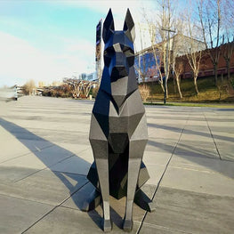 Geometric dog sculpture in an outdoor setting with a building and trees in the background.