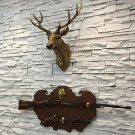 Deer head mount on a wall with two rifles displayed below against a stone-textured wall.