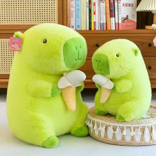 Two green plush toys resembling bears sitting on a light-colored surface with a wooden shelf and books in the background.
