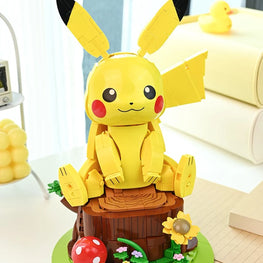 A yellow Pikachu-themed toy or model figure with large black-tipped ears, red cheek circles, and a smiling face, posed on a brown log base with small green, red, yellow, and pink decorative details in a bright indoor setting.