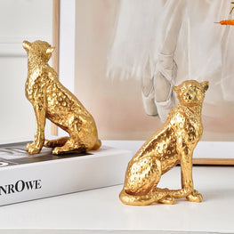 Two gold leopard figurines on a white surface with a blurred background