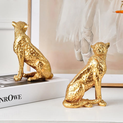 Two gold leopard figurines on a white surface with a blurred background