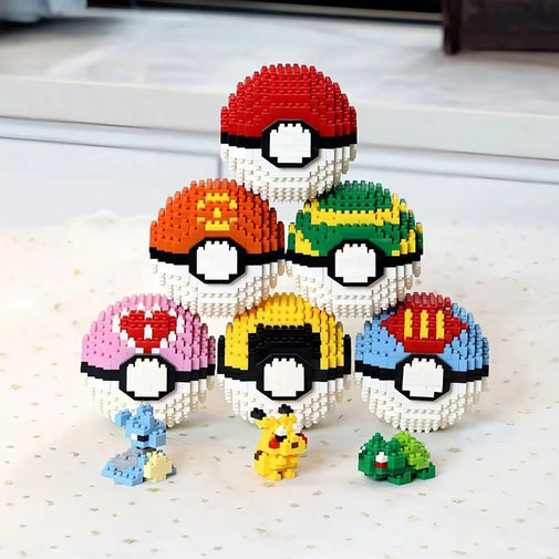 A set of seven Pokémon-themed bead ball models arranged in a pyramid on a light speckled surface, with small character figures placed in front. The balls feature various color schemes including red/white, orange/white, green/white, pink/white, yellow/white, blue/white, and a black/white center design.
