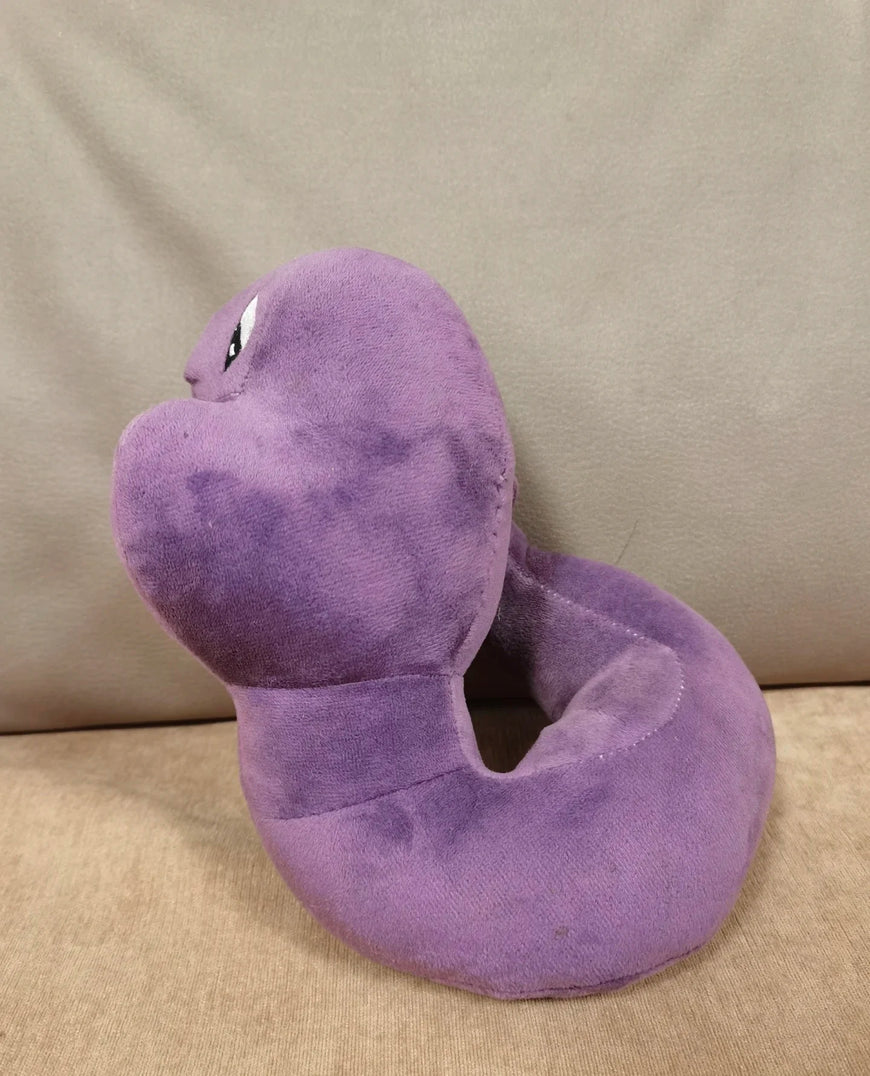 A purple plush snake-shaped neck pillow with embroidered eyes, resting on a beige fabric surface against a matching beige background.