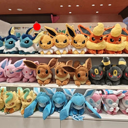 Three shelves filled with colorful plush toy Pokémon, including Eevee, Eevee variants, and other shiny-colored plushies, displayed in a store setting.