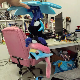 A person holds a stack of plush toys, including a blue winged character, a black cat-like plush, a pink bird-like plush, and another blue/yellow plush, in a cluttered home office or playroom with a pink chair, shelves, and computer desk visible.
