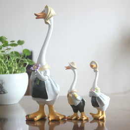 Three decorative goose figurines with a plant in the background