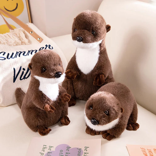 Three plush otters sitting on a surface with a 'Summer Vibes' pillow in the background.