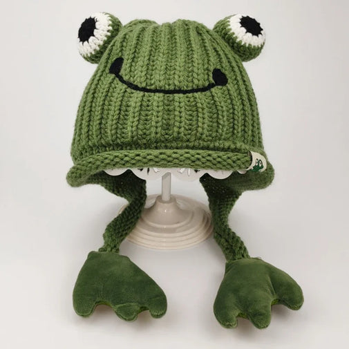 Green knitted frog hat with black eyes and a smile on a white background
