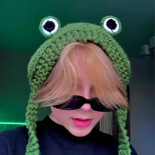 Person wearing a green frog-themed knitted hat with large eyes and black pupils.