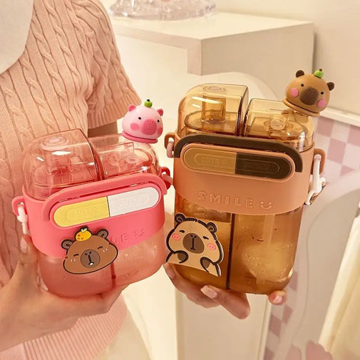 Two cute capybara-themed water bottles held in hands. The bottle on the left is pink with a yellow and white button, and a cartoon capybara sticker.