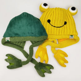 Green frog-themed beanie with textured texture and yellow frog-themed beanie with smiley face and hands on a white background