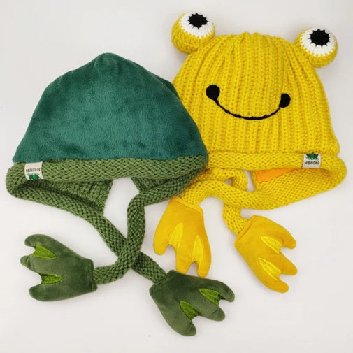 Green frog-themed beanie with textured texture and yellow frog-themed beanie with smiley face and hands on a white background