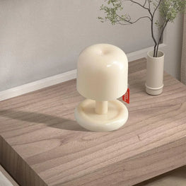 White mushroom-shaped lamp on a wooden surface with a plant in the background