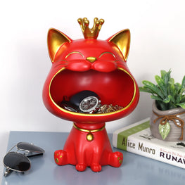 Red cat-shaped jewelry organizer with a gold crown on a surface with books and sunglasses.