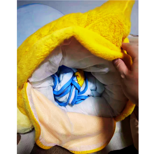 A close-up of a yellow plush blanket or pillow being opened by a hand, revealing a soft white inner lining and folded blue and yellow fabric inside.