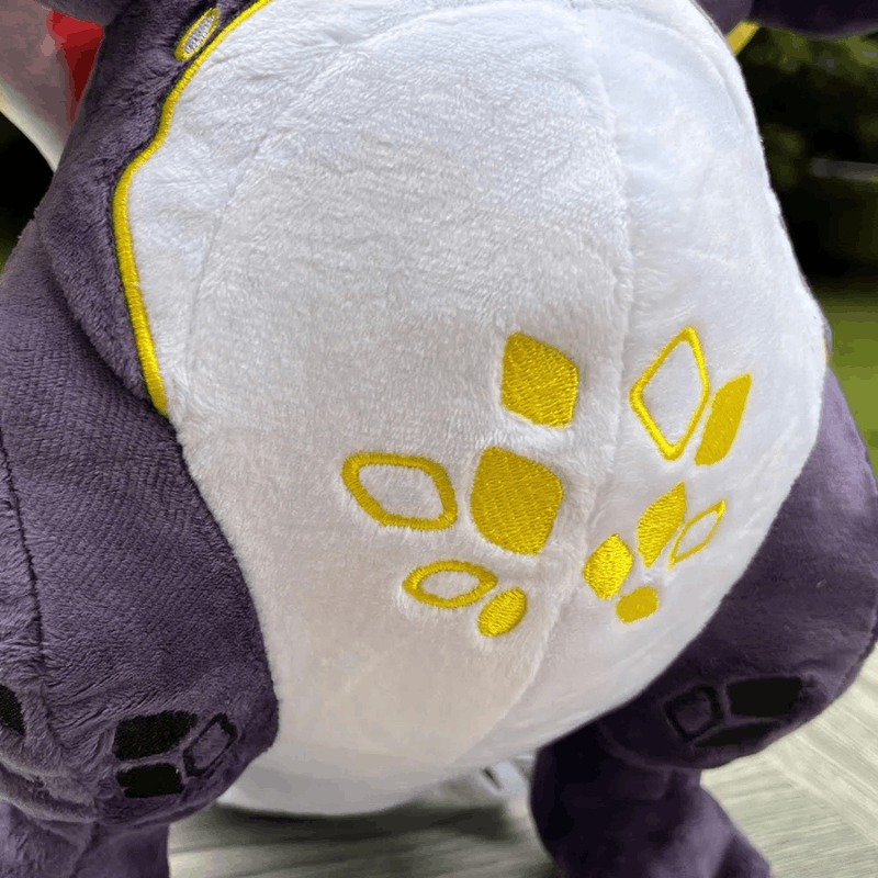 Close-up of a plush toy's back, featuring a white center with yellow embroidered paw-print details and purple sides.